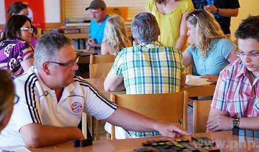 Mehrere Menschen sitzen am Tischen und spielen Qwirkle