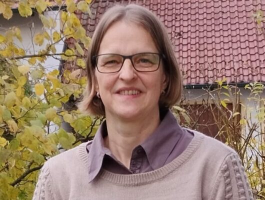 Frau mit Brille vor Baum und Haus
